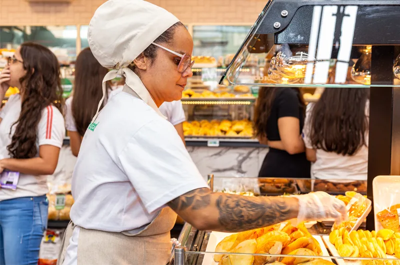 Funcionária do supermercado ababastecendo uma mesa quente com pratos prontos para consumo